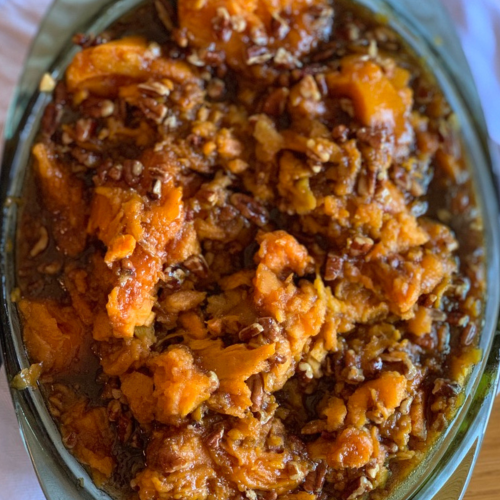 Sweet potatotes in a casserole dish seasoned with brown sugar, honey, cinnamon and nutmeg. Topped with toasted pecans.