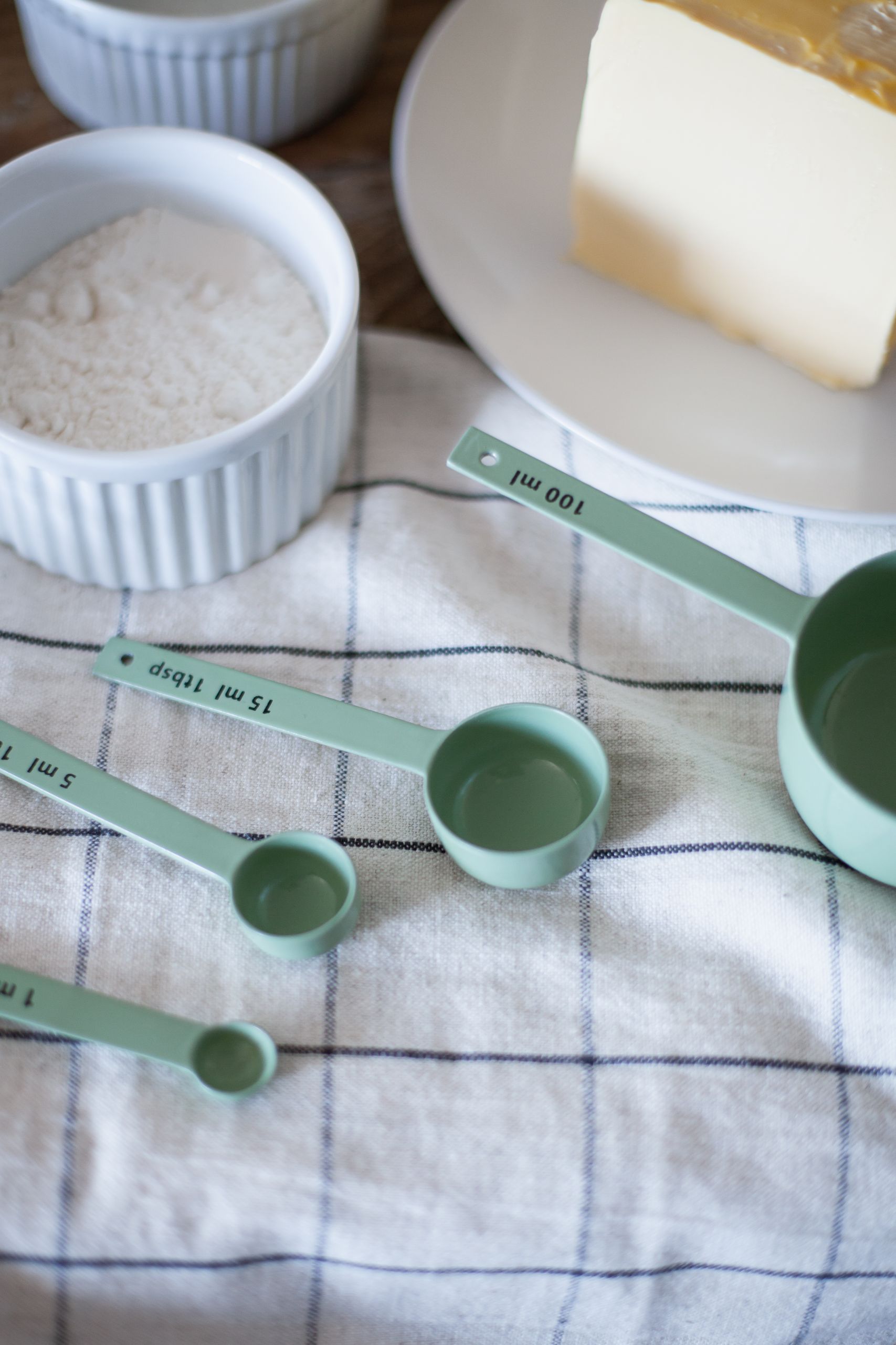 Close-up of baking essentials including butter, flour, and measuring spoons on a cloth.